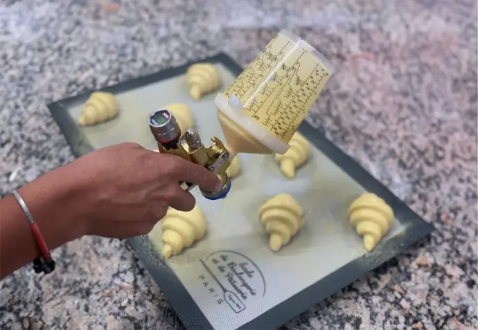 Pistolet SATAjet 1000 B RP Pastry Edition pulvérisant sur des croissants avec godet RPS